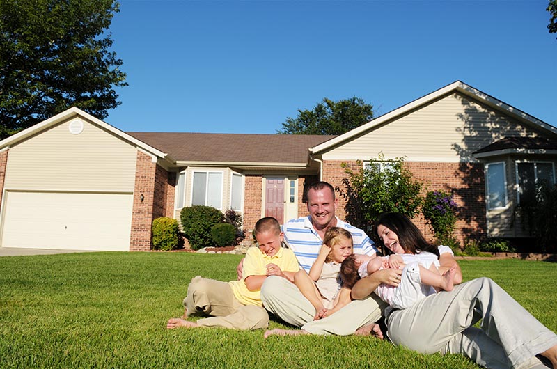 Happy family of five sitting in the yard in front of their house.