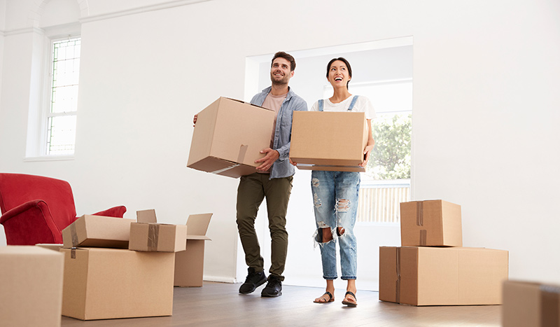 Happy woman and man carrying moving boxes into their new home.